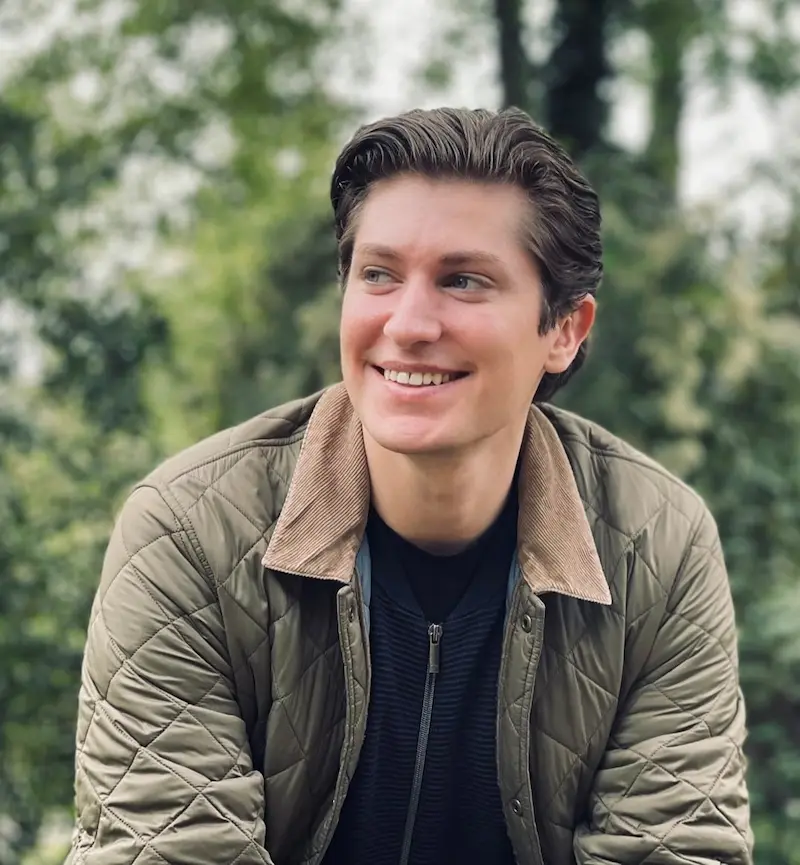 Portrait of Maximilian Artelt, smiling warmly in front of a green