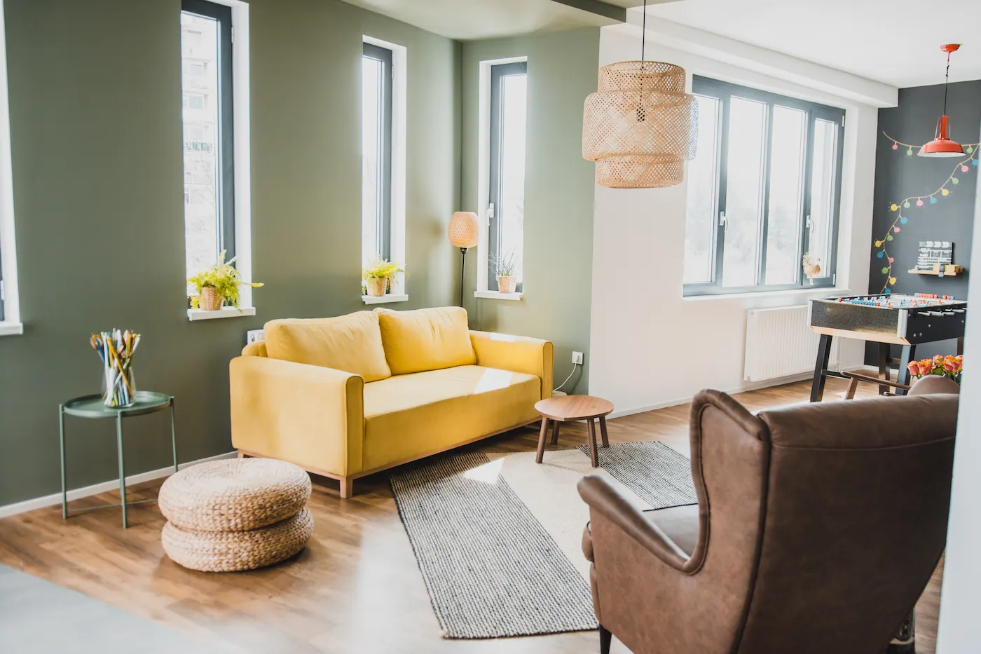 Stilvolles Wohnzimmer mit gelbem Sofa und großen Fenstern und einem Kicker im Hintergrund