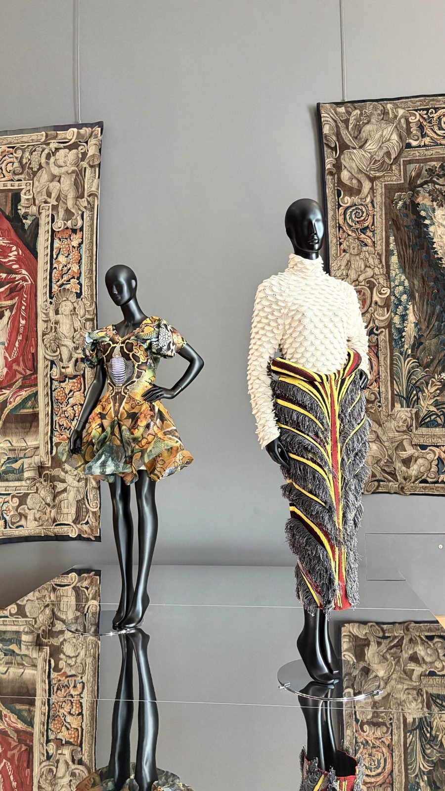 Kunstvolle Gewänder auf stilvollen schwarzen Mannequins in einer Galerie mit großen Gemälden und spiegelndem Boden im Louvre.