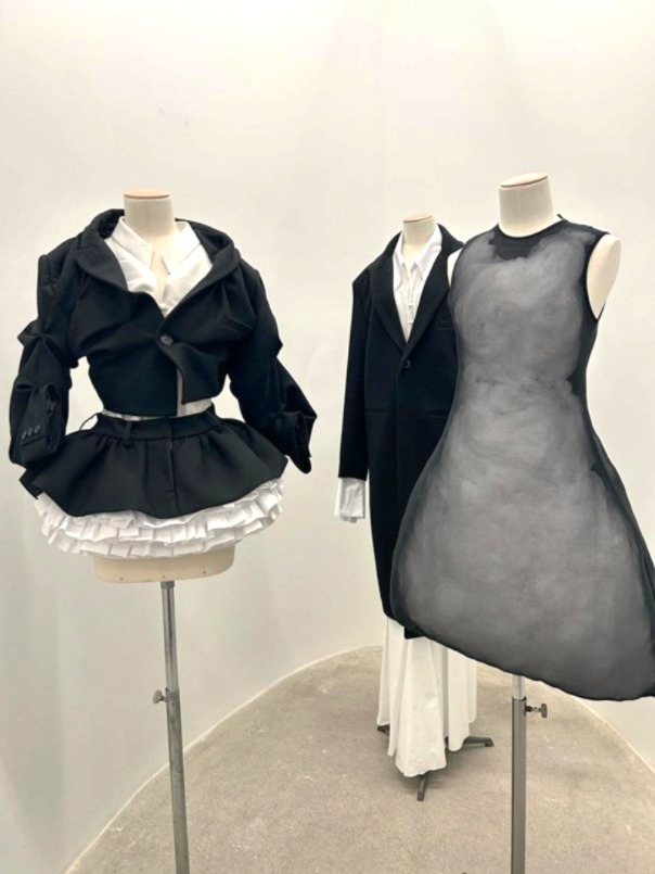 Drei schlichte, schwarze, kreative Kleider auf Schaufensterpuppen in einer Modeausstellung, präsentiert auf Büsten in einer ovalen Nische.
