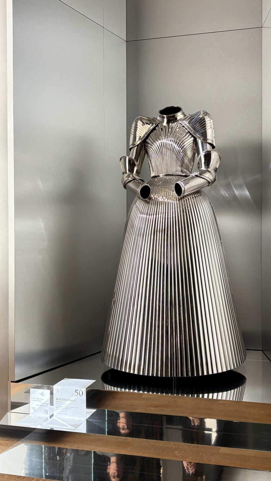 Ein futuristisches Haute-Couture-Metallkleid mit Falten von Balenciaga, das in einem modernen Ausstellungsraum präsentiert wird.