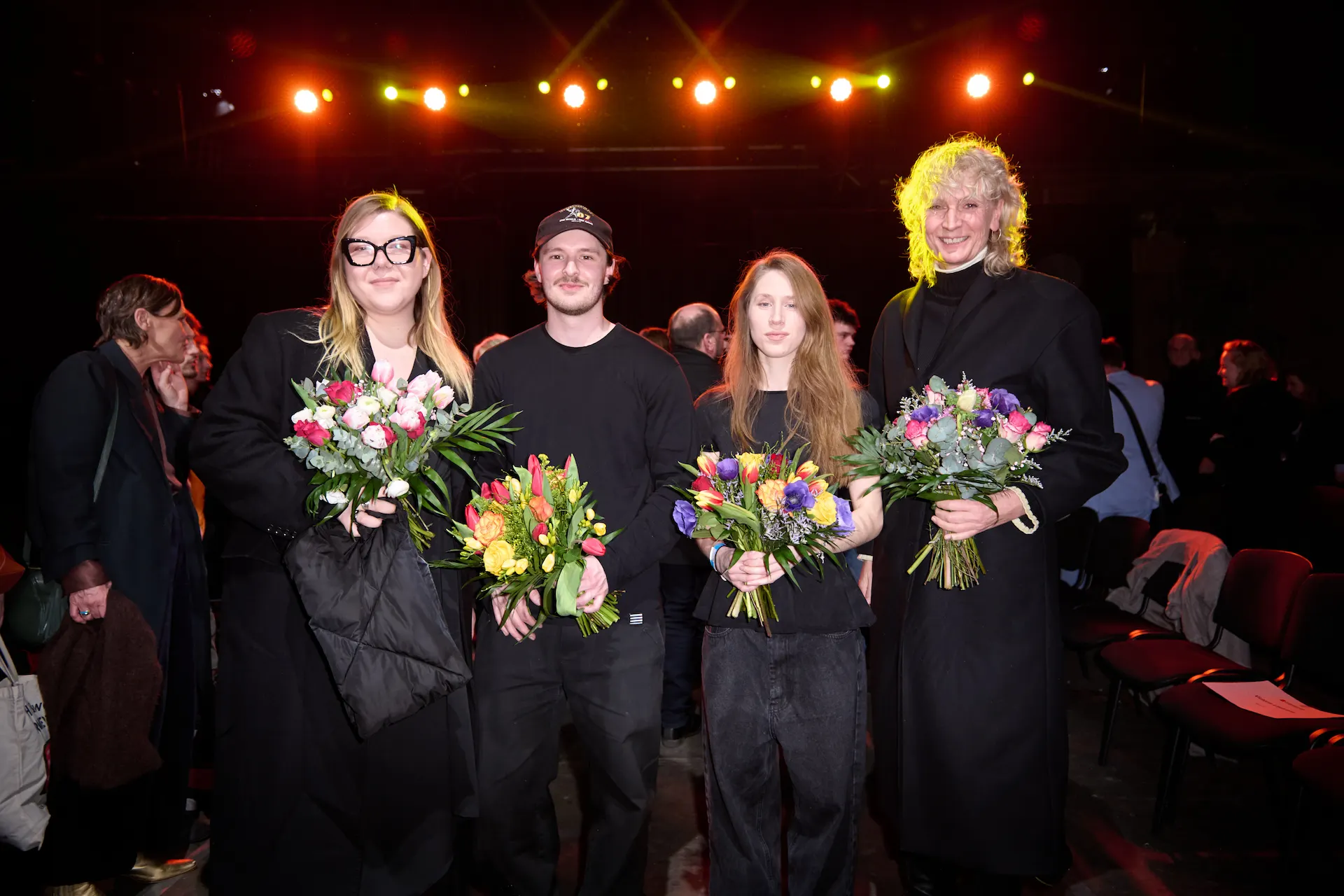 Eine Gruppe von vier Personen, die mit Blumen posieren, während sie auf dem Laufsteg der Stage Modenschau stehen.