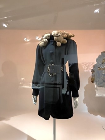 Eleganter schwarzer Damenmantel mit einzigartigem Kragen aus kleinen Teddybären, im Schaufenster mit Spot beleuchtet.