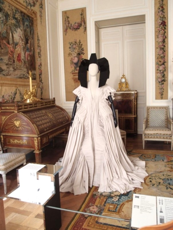 Ein elegantes Haute-Couture-Kleid in Weiß von Rick Owens in einer Ausstellung, umgeben von historischem Dekor.