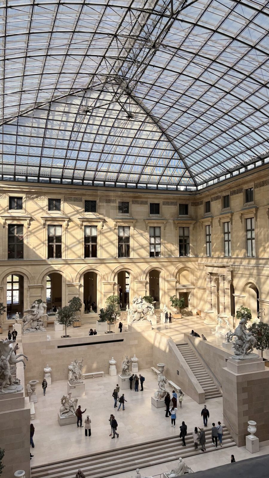 Beeindruckende Innenansicht des Louvre mit Glasdach und Skulpturen.