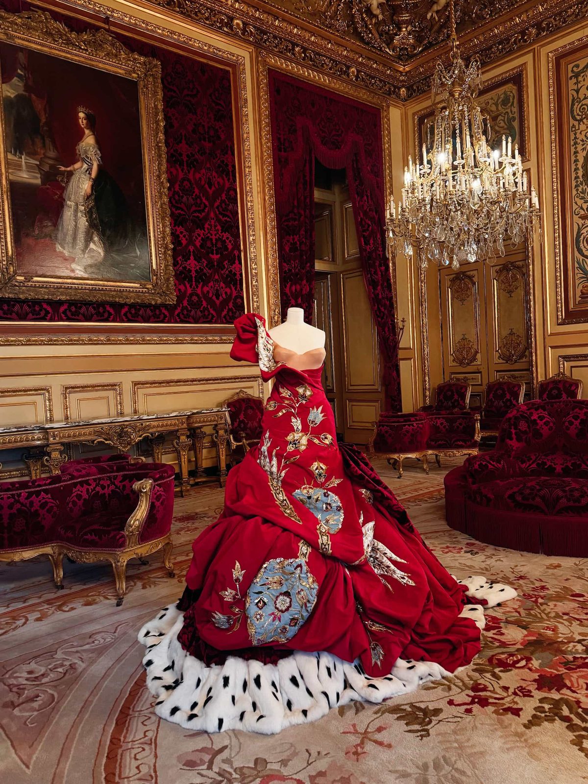 Präsentation eines eleganten Christian-Dior-Kleides in einem majestätischen Raum mit antiken Möbeln, großen Gemälden und prächtigen Kronleuchtern, die an einen Palast erinnern.