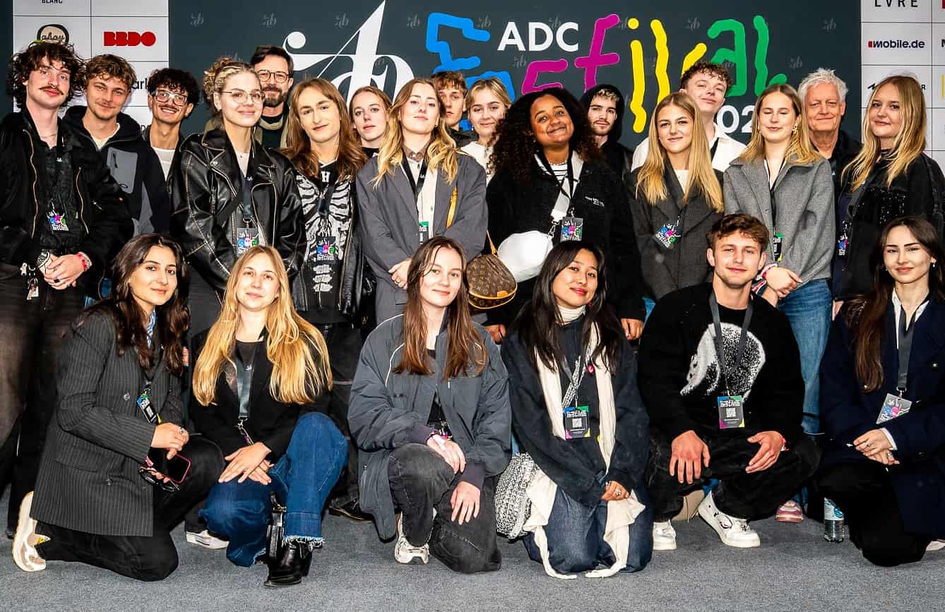 Gruppenfoto von glücklichen AMD-Studierenden des Studiengangs Marken- und Kommunikationsdesign vor dem Plakat des ADC Award 2025.