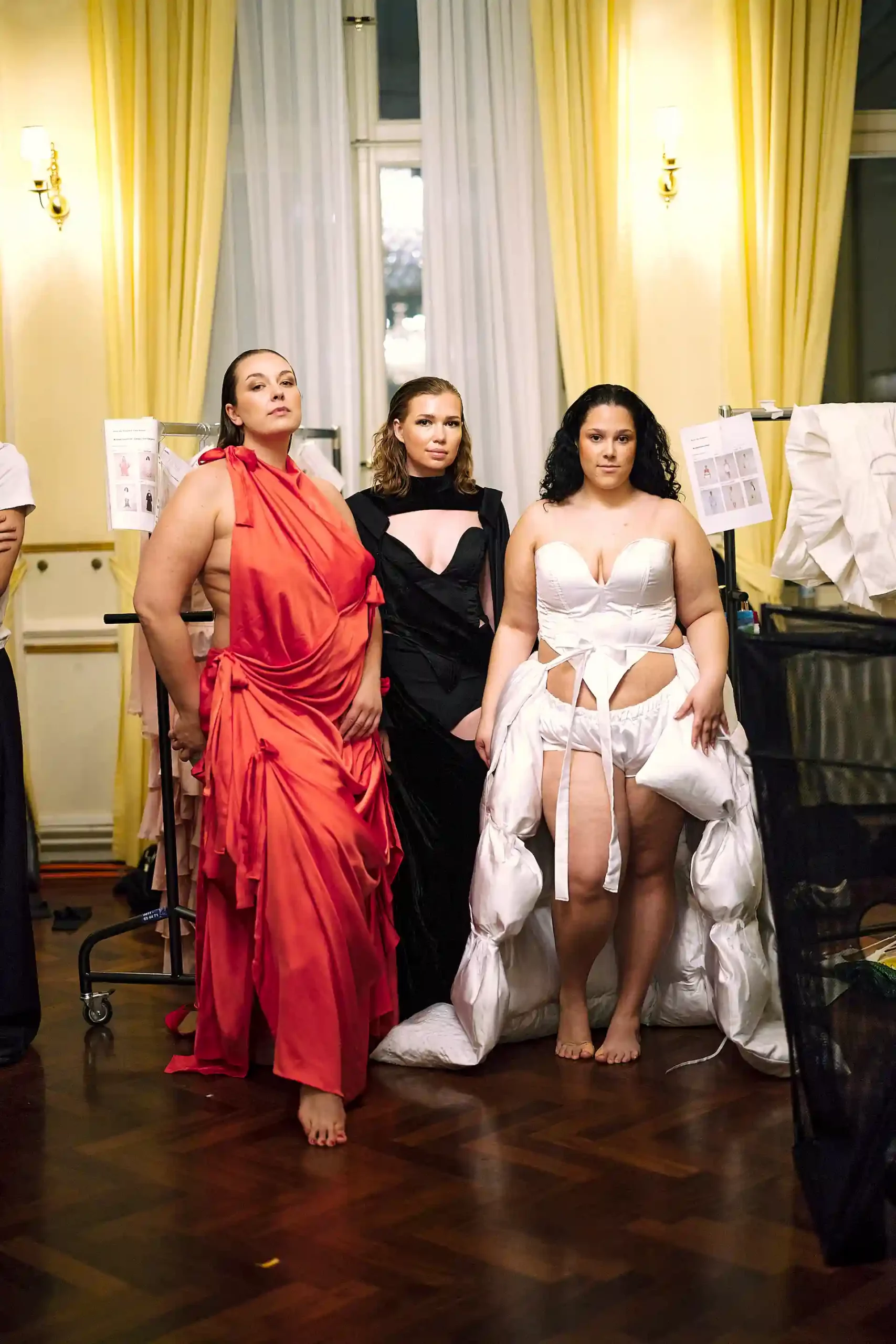 Ein Blick hinter die Kulissen: Drei Frauen in eleganten Kleidern, die Selbstsicherheit und Stil verkörpern.