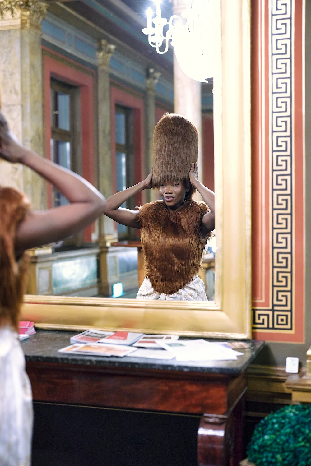 Model (People of color) zeigt einzigartigen Haarstil vor einem großen Spiegel in einem eleganten Raum.