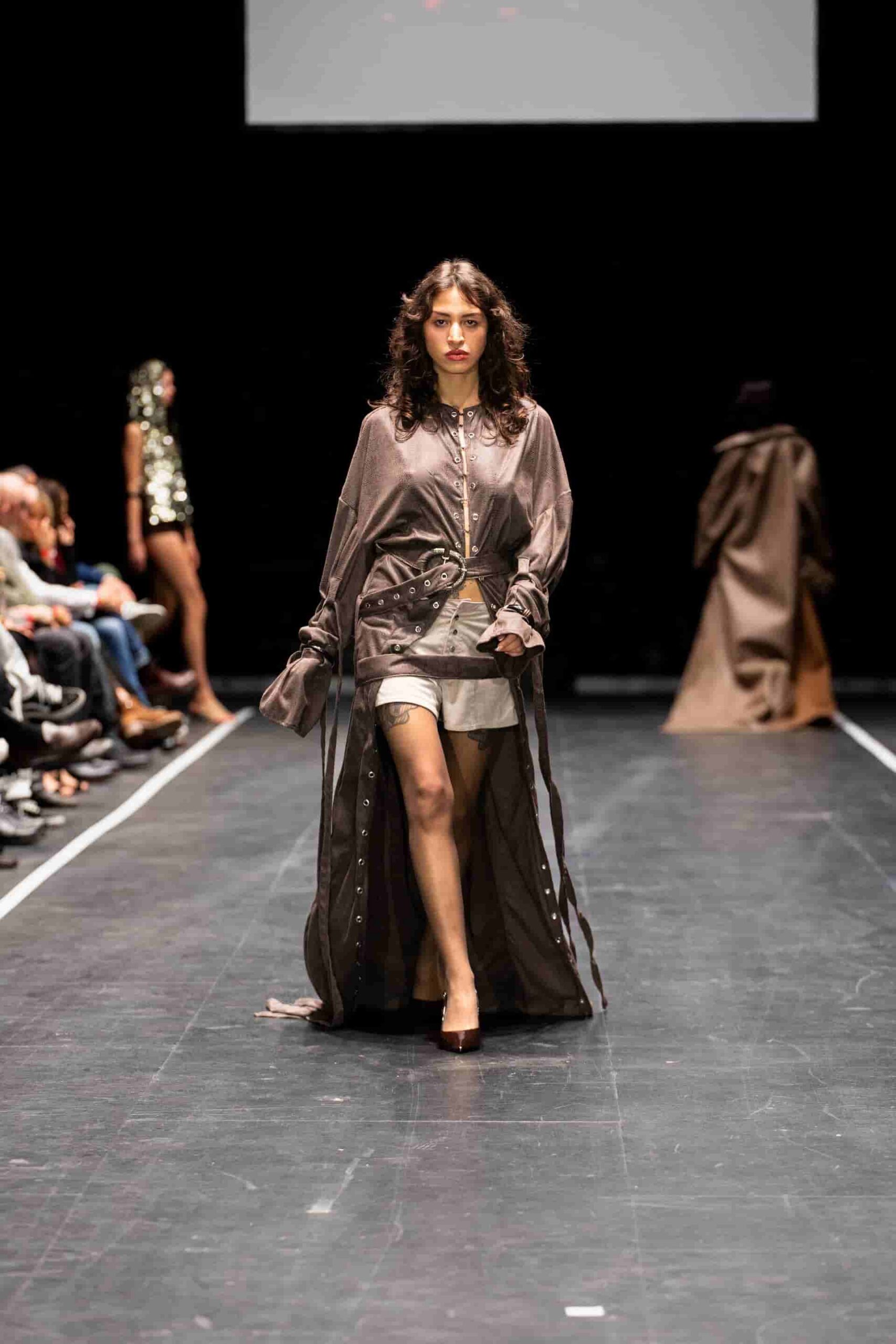 Laufstegaufnahme eines Models in brauner Kleidung.