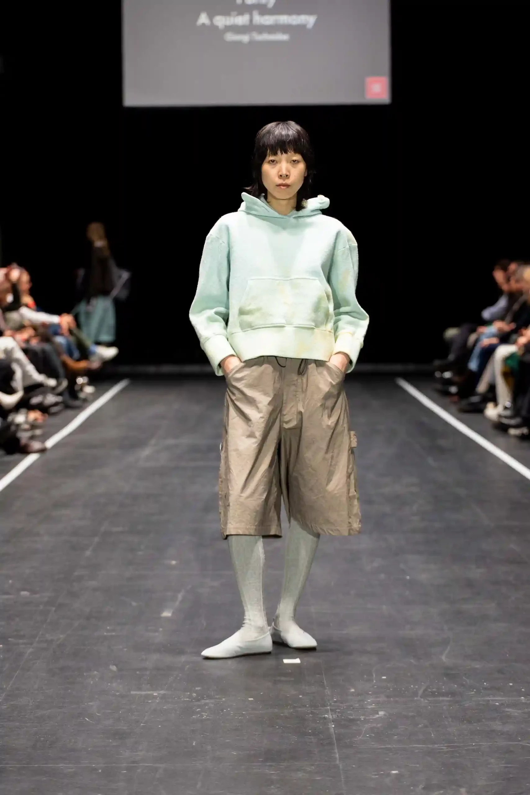 Aisatisches Model auf dem Laufsteg in einem mintgrünen Hoodie und beigen Shorts