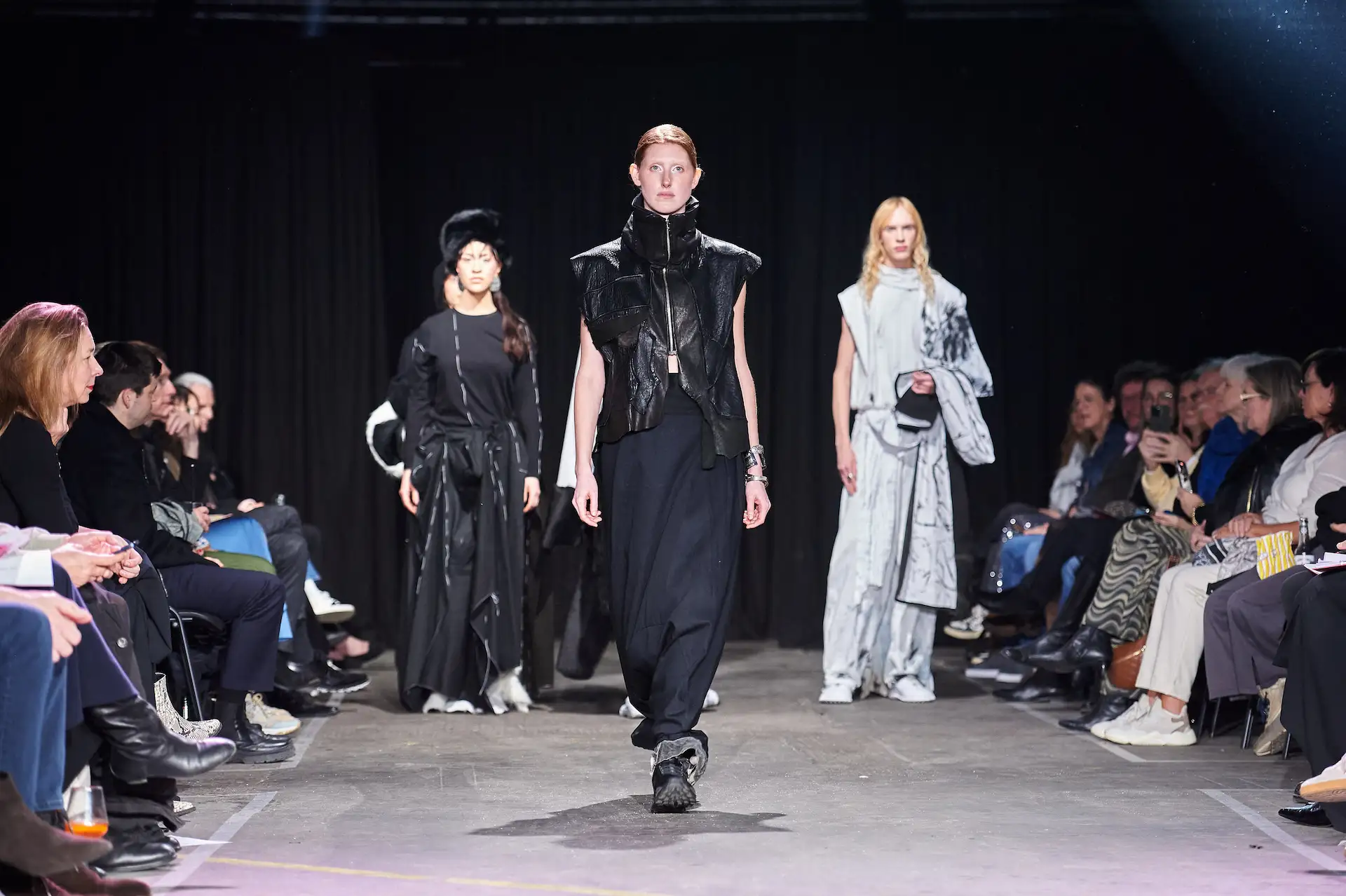 Drei Modelle präsentieren moderne Mode, schwarz und weiß, auf dem Laufsteg während einer Modenschau.