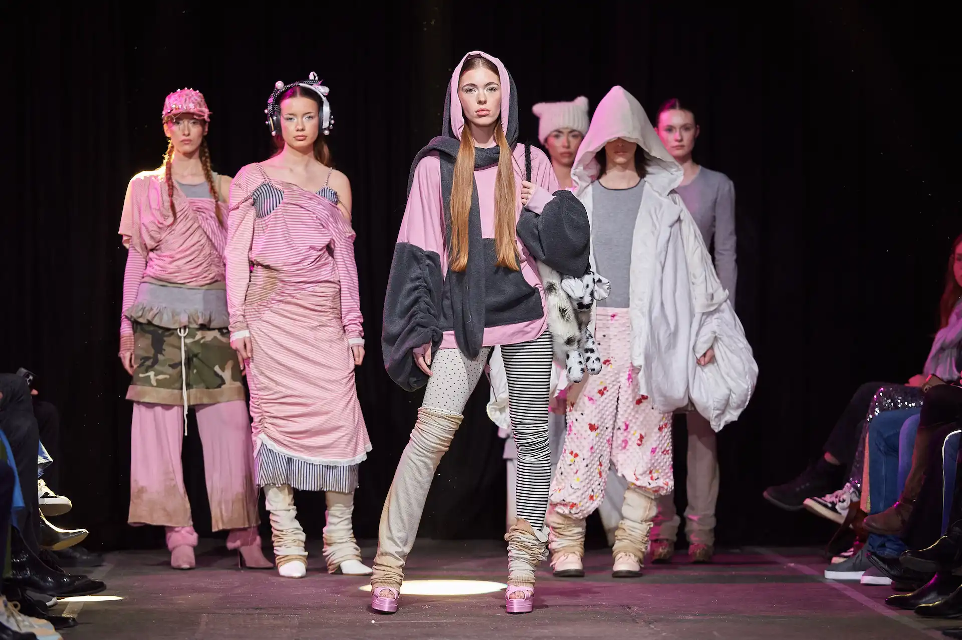 Sechs Models auf dem Catwalk präsentieren moderne Mode in Rosa, Weiß, Rot und Grau, mit Akzenten und teils mit, teils ohne Kopfbedeckung. Es wirkt wie eine Märcheninszenierung, dabei dennoch modern und lässig.
