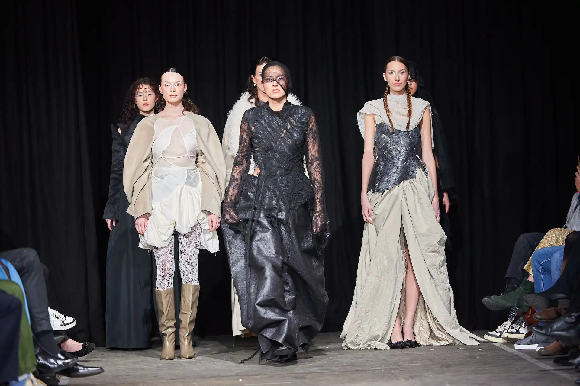Sechs Models auf dem Catwalk präsentieren avantgardistische Kleider in Schwarz und Weiß, teils aus Spitze.