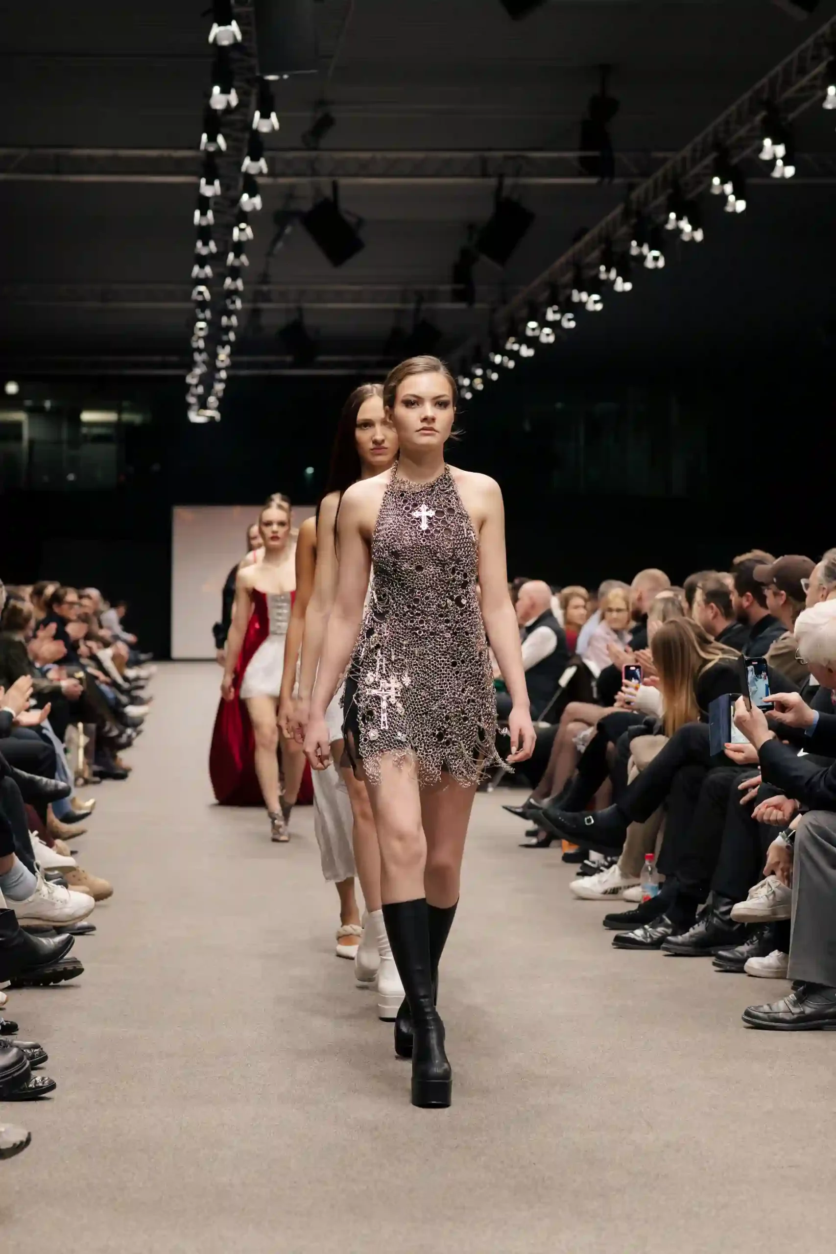Models auf dem Laufsteg präsentieren elegante Kleider während das Publickum begeistert zuschaut.