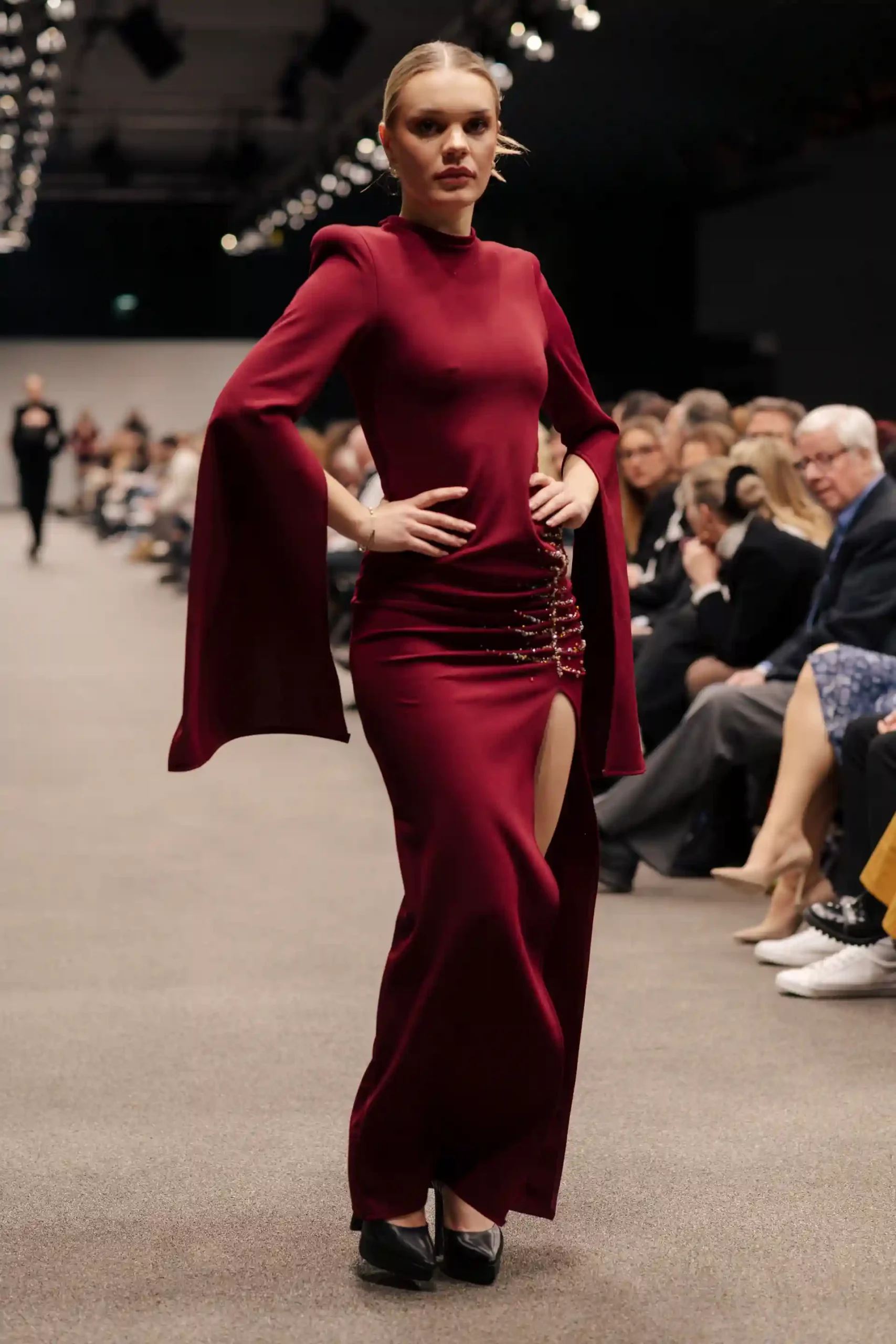 Model präsentiert ein elegantes rotes Abendkleid mit seitlichem Schlitz und goldenen Details.