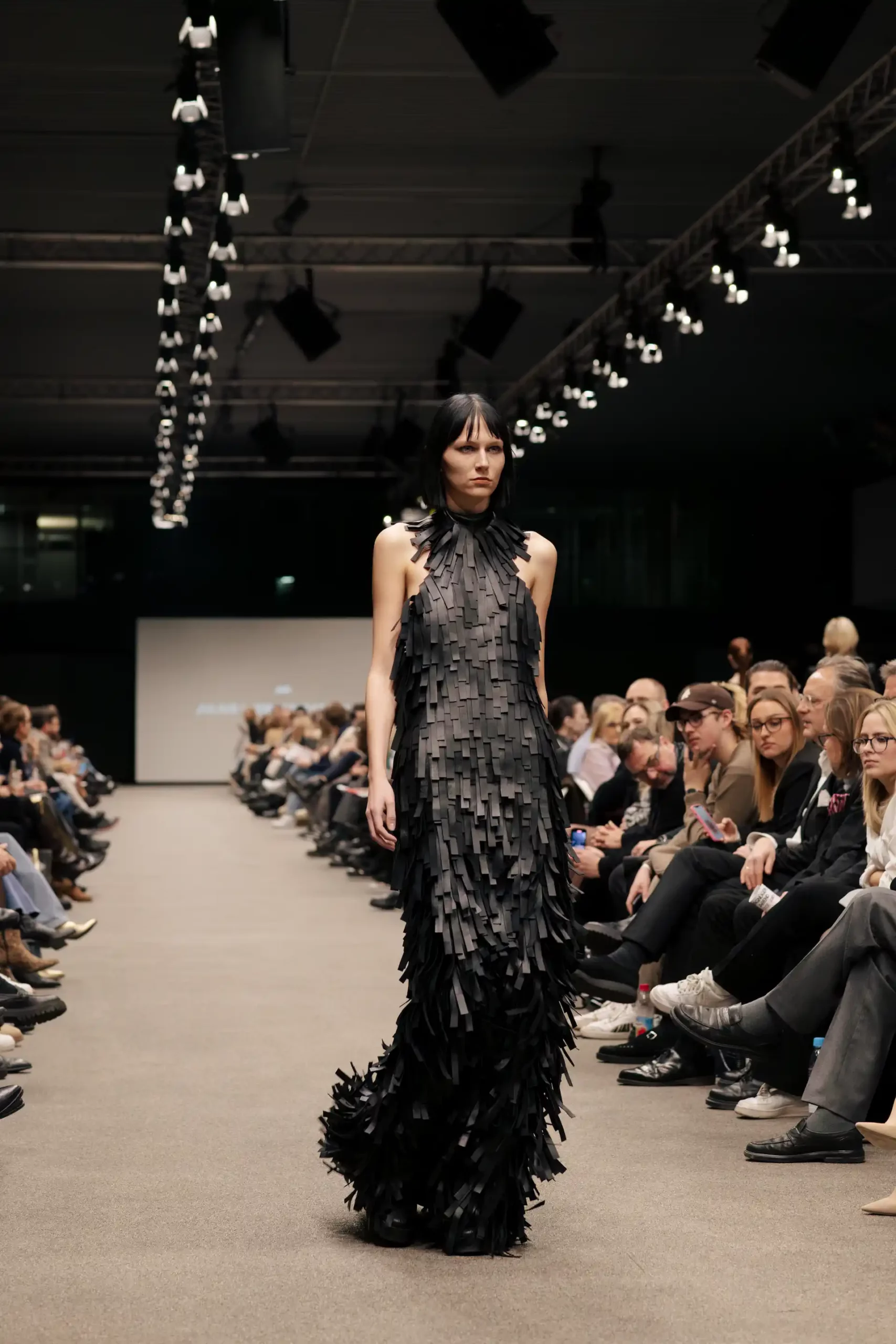 Eine elegantes Model in einem schwarzen Fransenkleid auf dem Laufsteg.