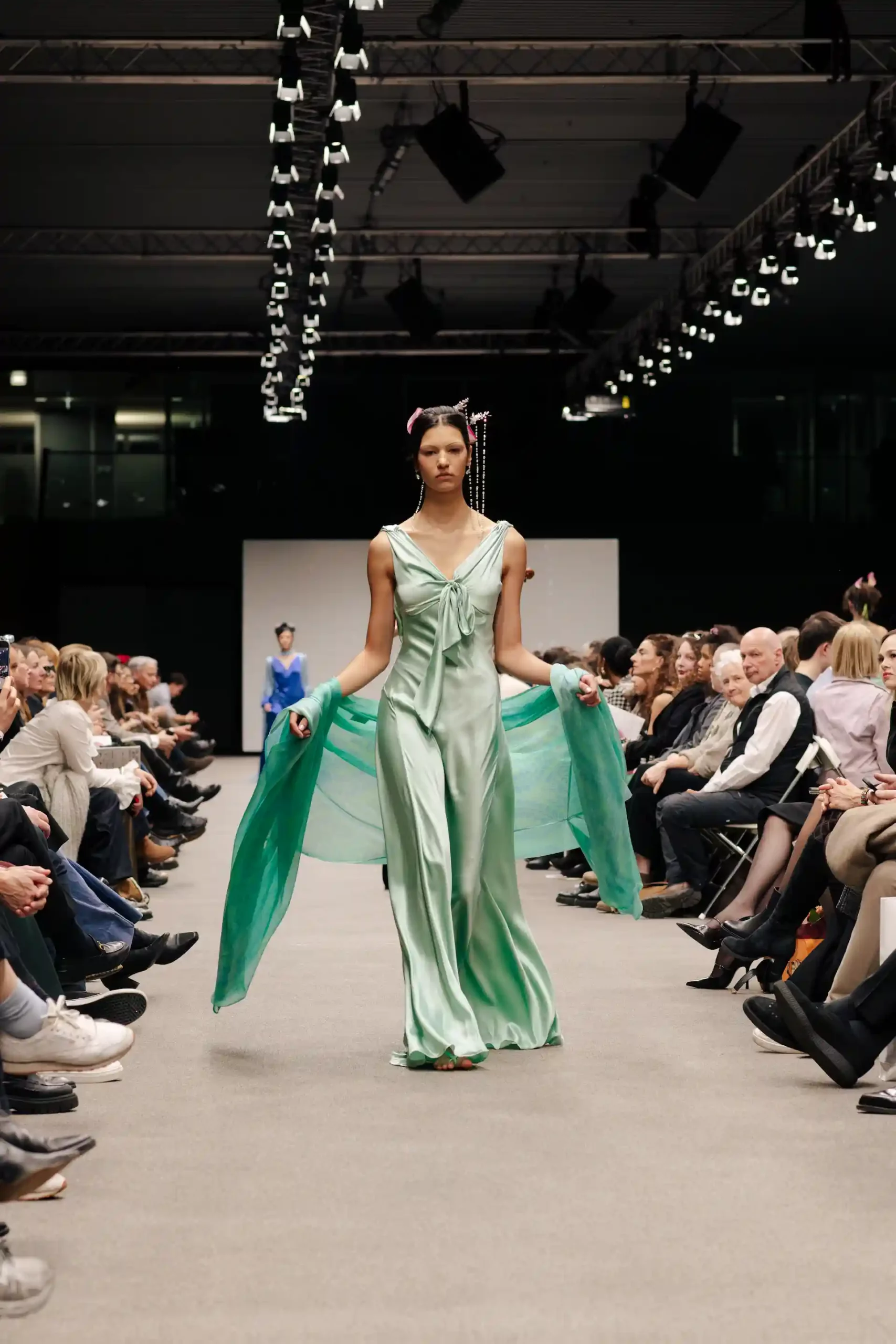 Elegantes Model auf dem Laufsteg, das ein grünes Kleid und einen Schal präsentiert.