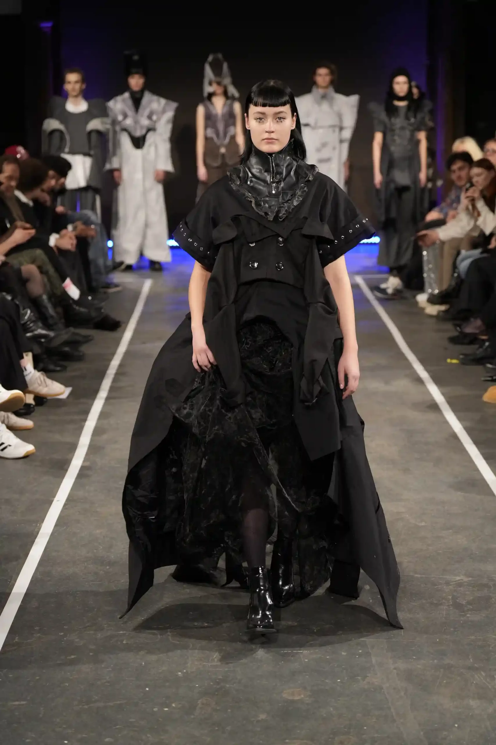 Avantgarde-Modepräsentation mit einem Model in einzigartiger schwarzer Kleidung auf dem Laufsteg.
