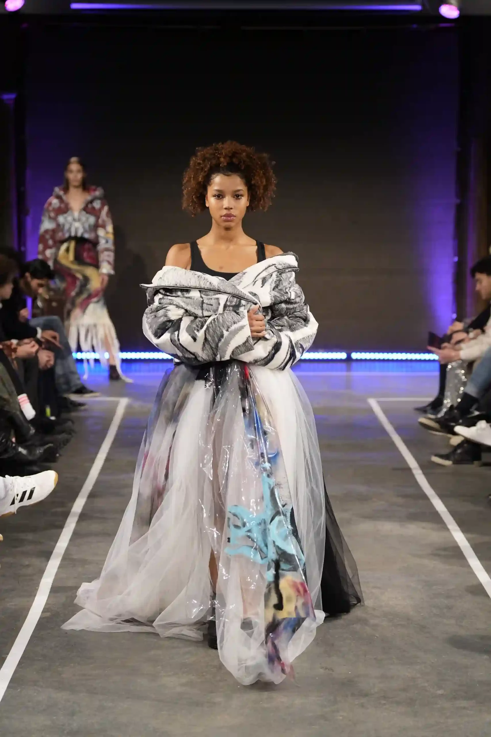 Model mit künstlerisches Kleid, mit transparentem Stoff auf dem Laufsteg.