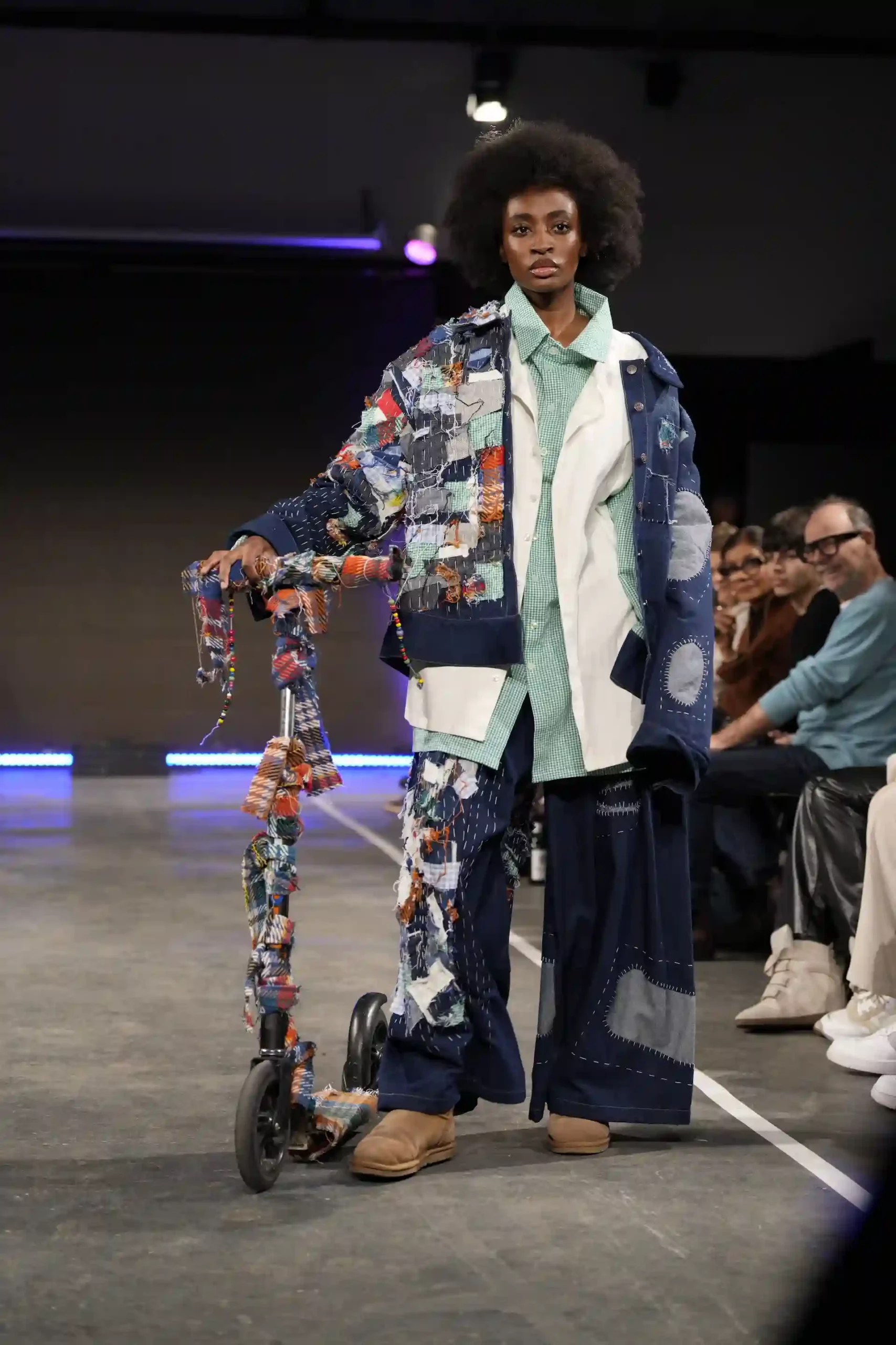 Ein People-of-Color-Model trägt ein buntes Denim-Patchwork-Outfit und fährt mit einem Roller über den Laufsteg.