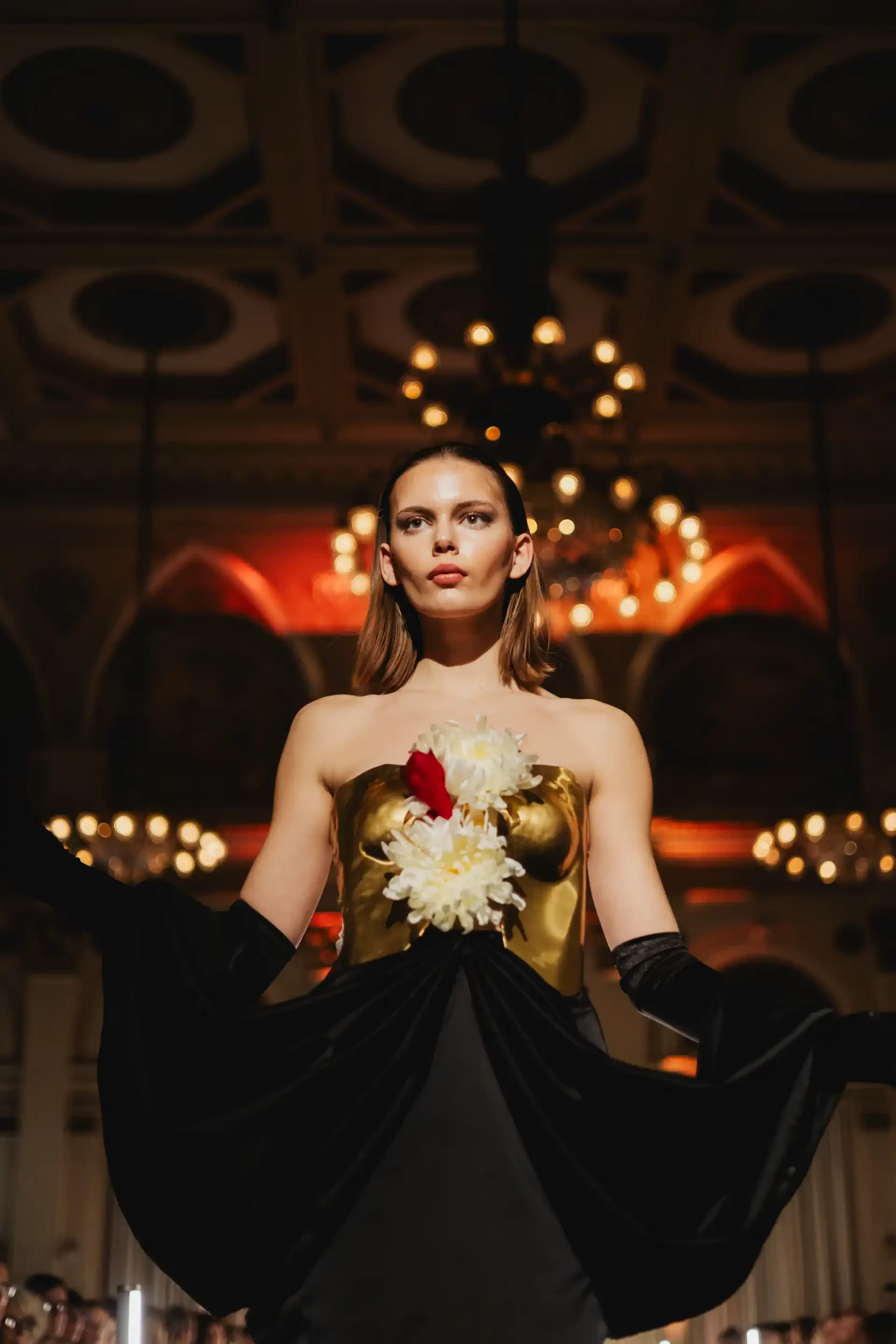 Modell auf einem eleganten Modeschau mit goldener blumenverzierter Bluse und schwarzem Rock.