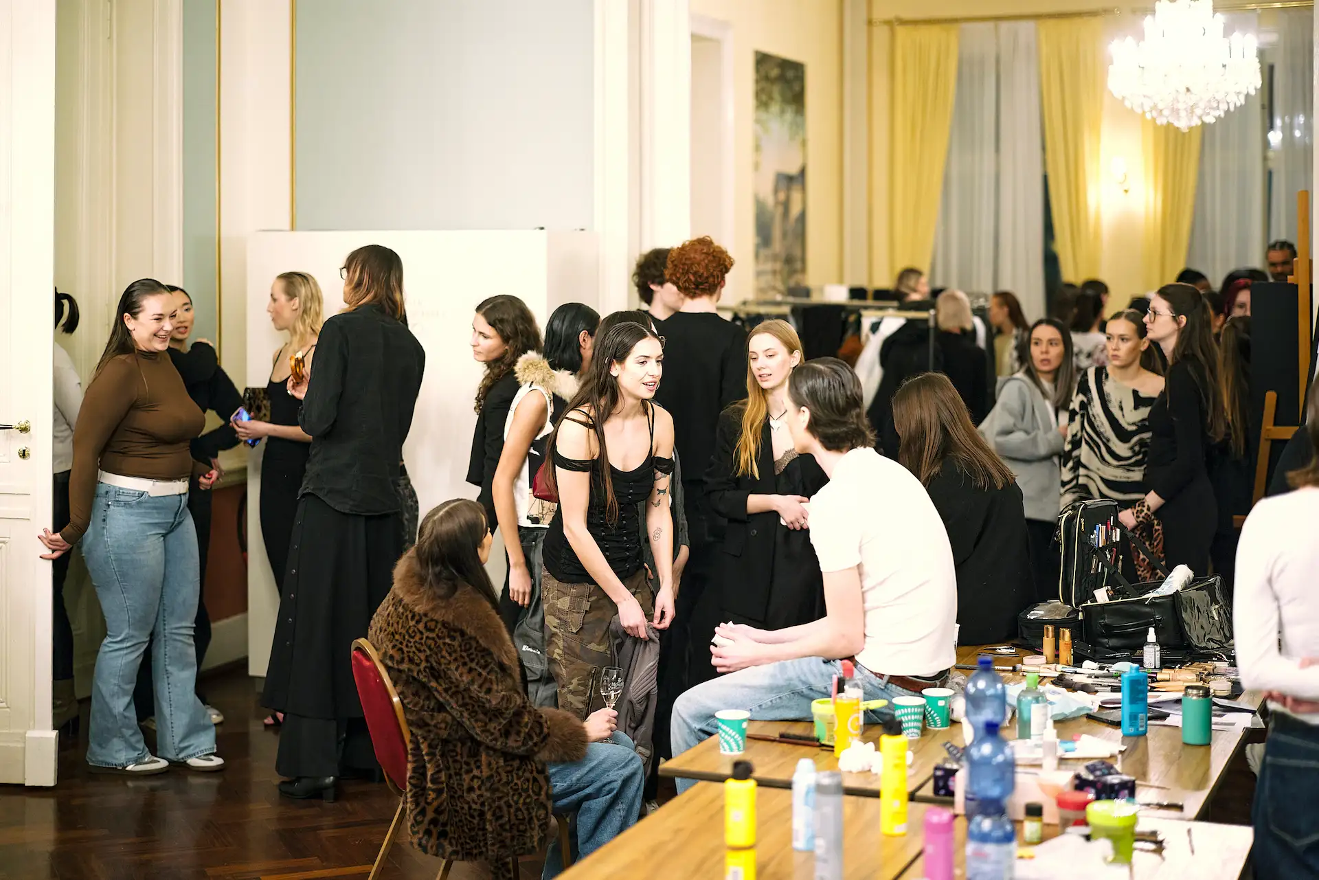 Ein Blick hinter die Kulissen der Modenschau: eine kreative Atmosphäre mit Models, Stylisten und Studierenden bei der Arbeit.