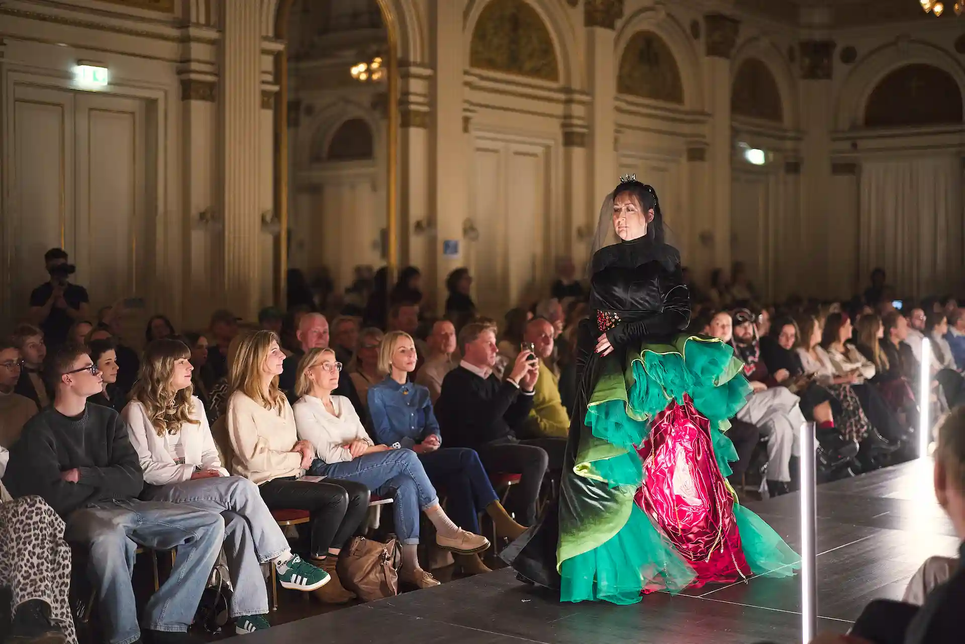 Model trägt Designer-Kreation auf dem Laufsteg mit lebendigen Farben und Details und einem fesselnden Publikum.