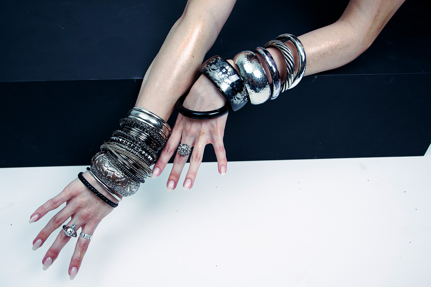 Hände mit silbernen Metallic-Handschuhen und Schmuck vor schwarzem Hintergrund