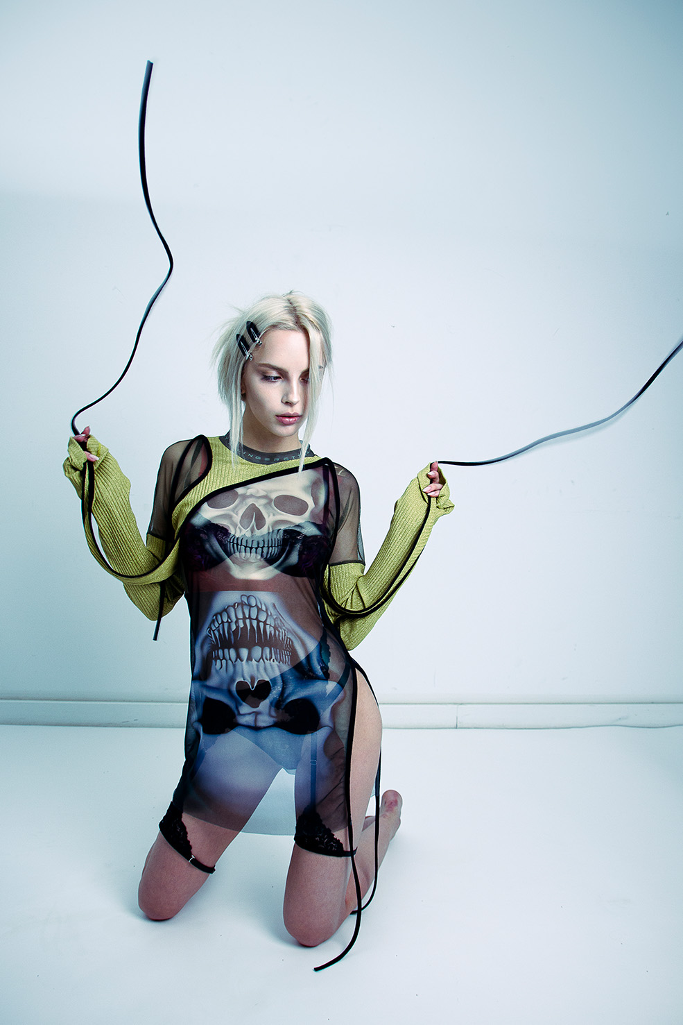 Model kniet in bedrucktem Longsleeve zwischen schwarzen Kabeln auf weißem Studioboden