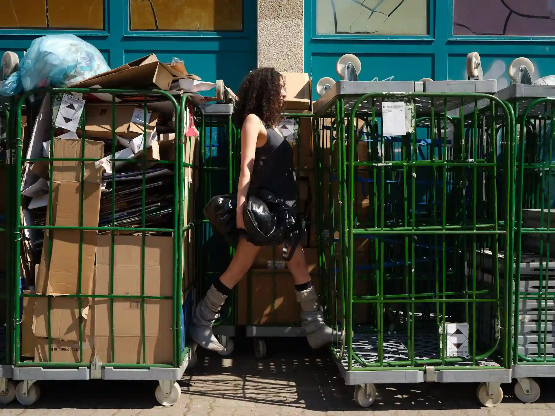 Model posiert an grünem Gitterkäfig im urbanen Außenraum