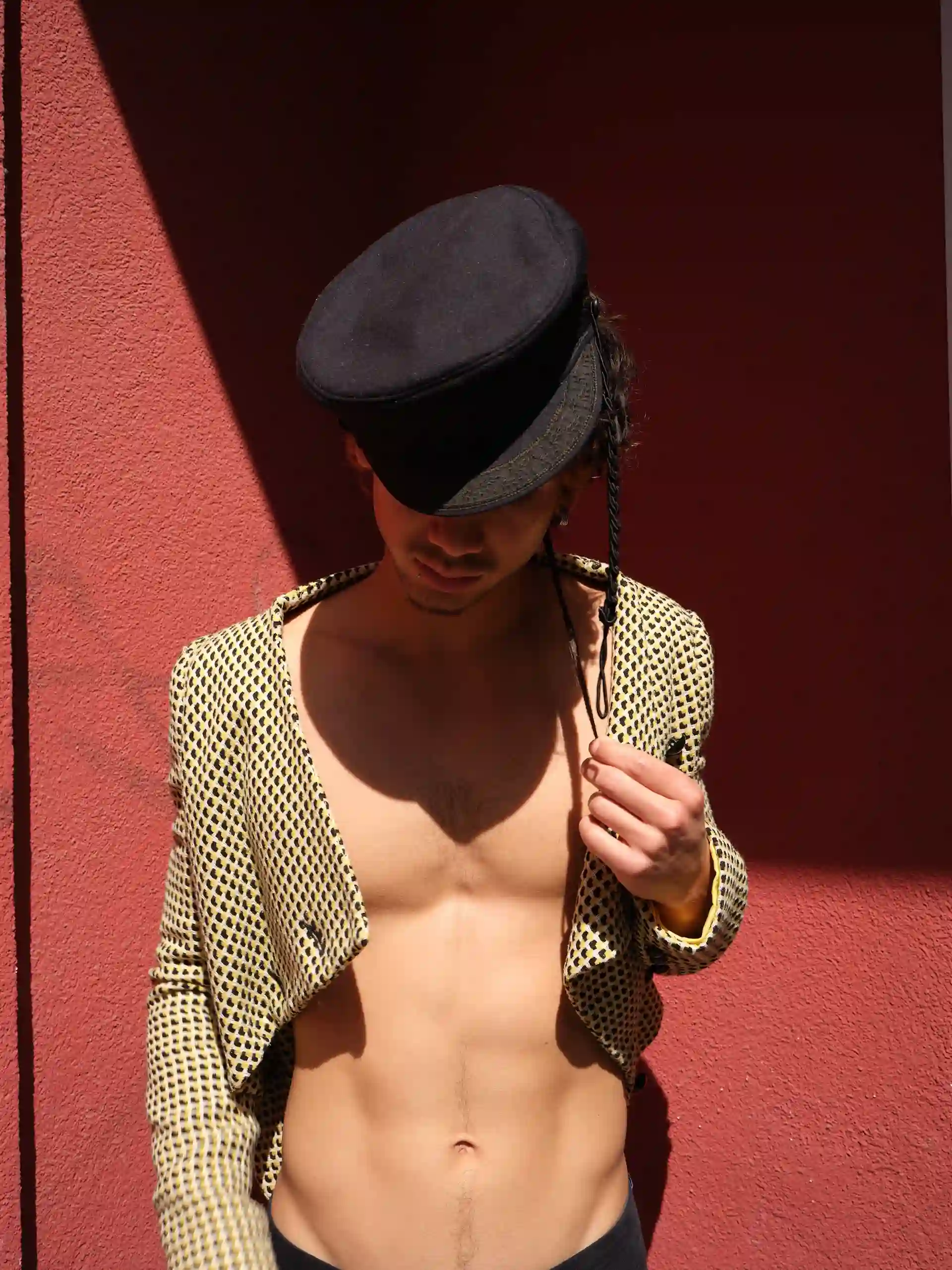 Model mit heller Schirmmütze und offenem dunklem Blazer vor roter Wand