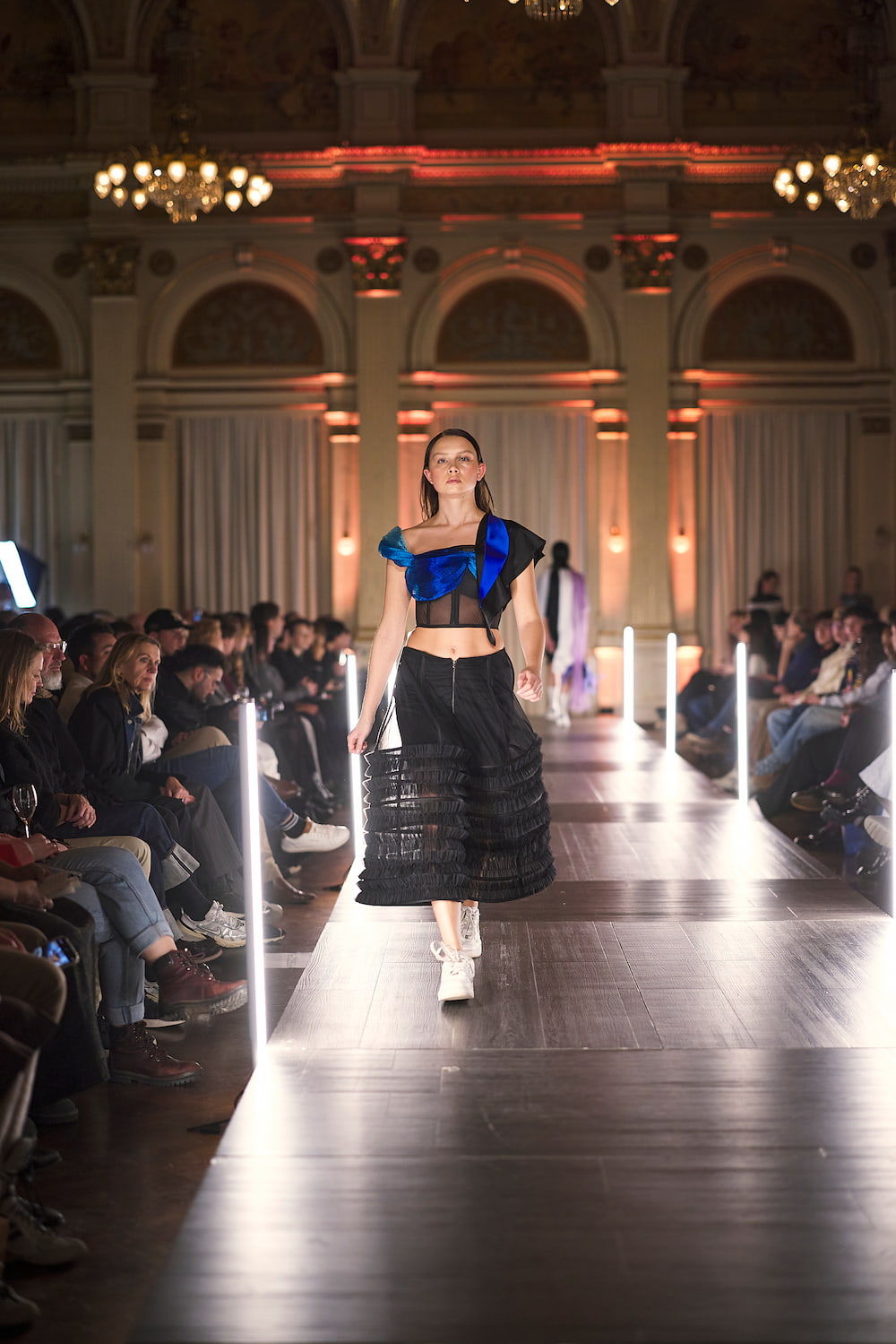 Modell trägt ein auffälliges blaues Top und einen schwarzen Rock auf dem Laufsteg