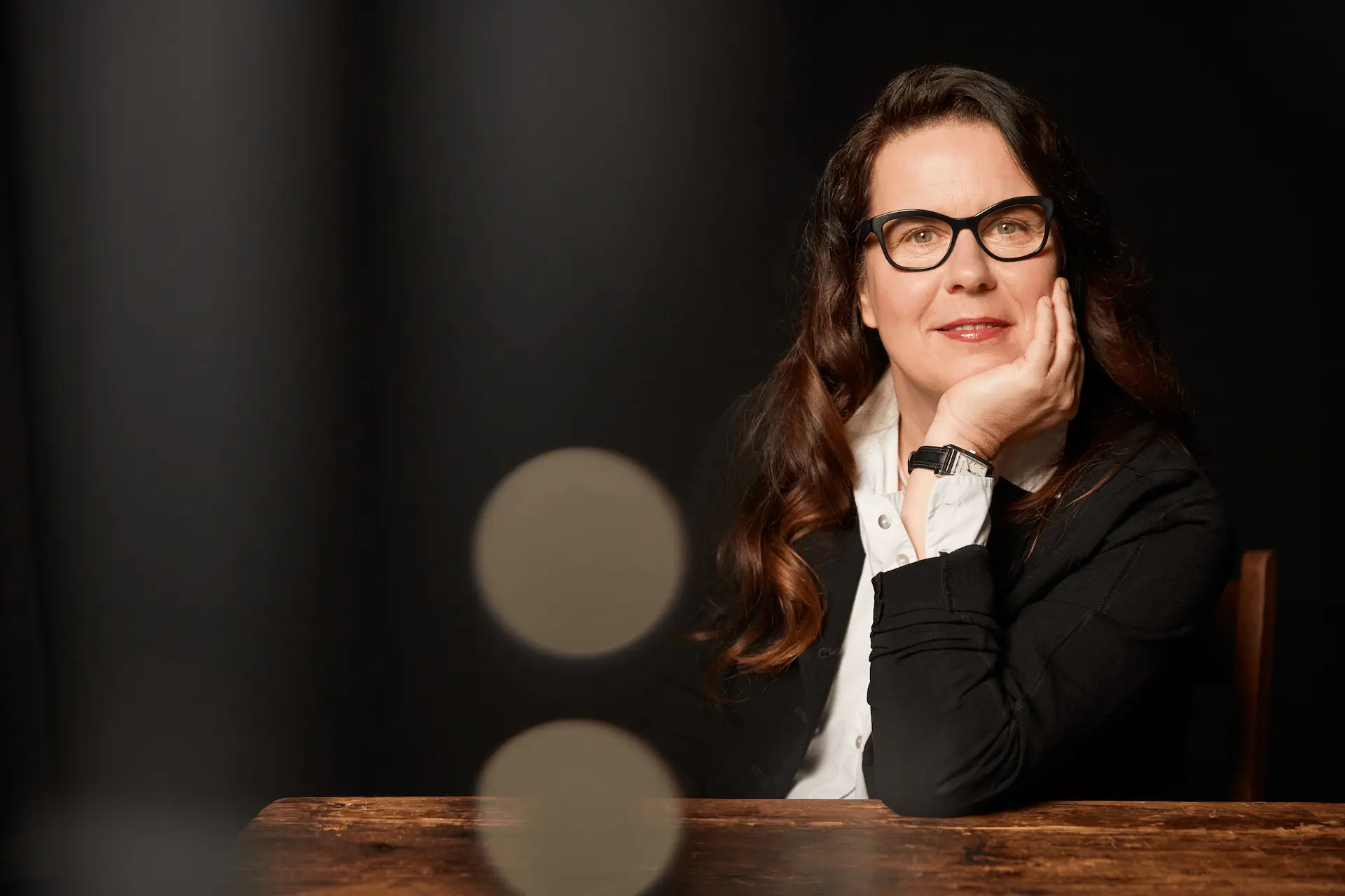 Porträt von Professorin Ulrike Nägele, die freundlich lächelnd an einem Holztisch sitzt.